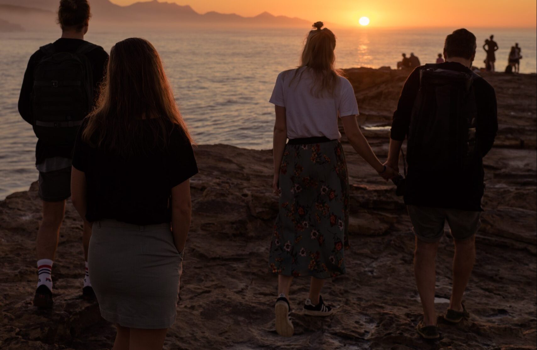 a group of couples standing at beach during sunset